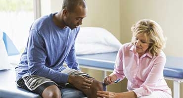 Physical therapist examining patient, testing reflexes with reflex hammer