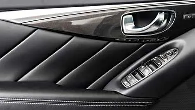 Close-up of a car's interior door panel: black leather with diagonal padding, chrome handle, and window/lock controls on the armrest.