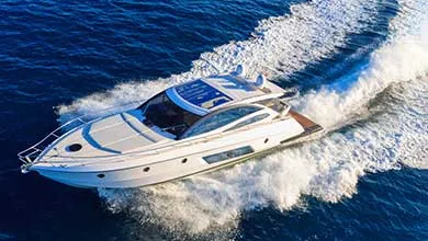 Aerial view of a white luxury yacht speeding across deep blue water, leaving a large white wake behind.