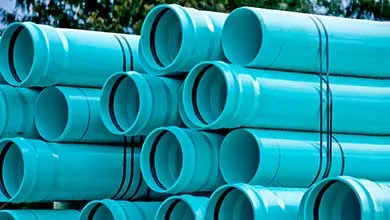 Several large teal PVC pipes are stacked in rows and secured with black straps.