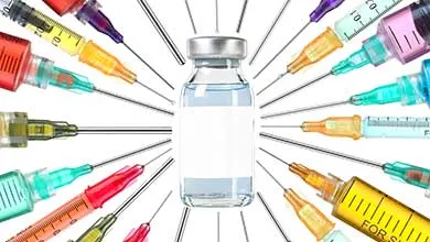 A glass medical vial with a blank label is surrounded by multiple syringes filled with colorful liquids, all with needles pointing toward the vial.