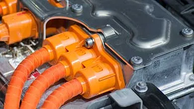 Close-up of electric vehicle battery components with orange high-voltage cables and connectors.