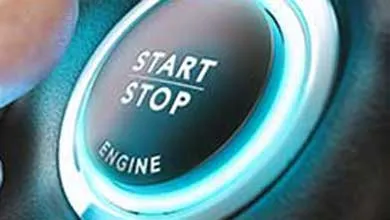 A person’s index finger presses a circular, blue-lit start-stop engine button on a car dashboard.