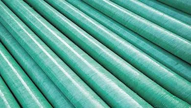 Close-up, diagonal view of large green industrial pipes arranged in parallel rows.