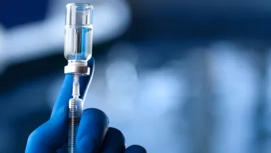 Gloved hand holding a syringe and vial in a medical or laboratory setting.