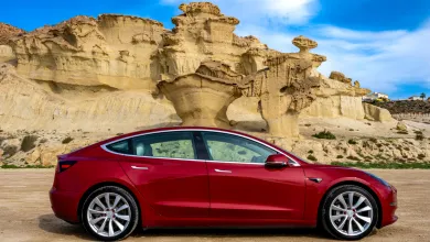 red electric car parked in front of rock formations in a desert landscape.