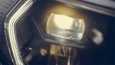 Close-up of a modern car headlight with the main bulb and adjacent LED strip illuminated.