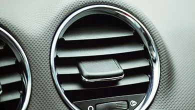 Close-up of a round car air vent with chrome trim on a textured gray dashboard.