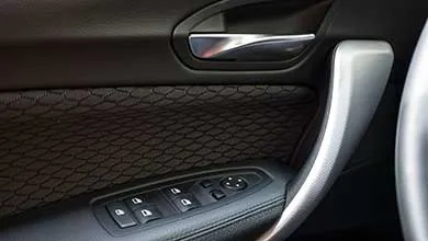 Close-up of a car door interior showing a chrome handle, black quilted leather, silver trim, and power window controls.