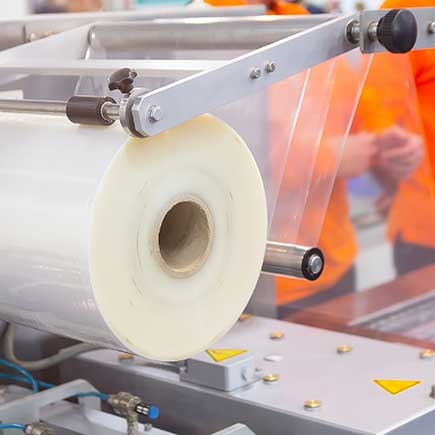 A machine with a large roll of plastic packaging film in a factory